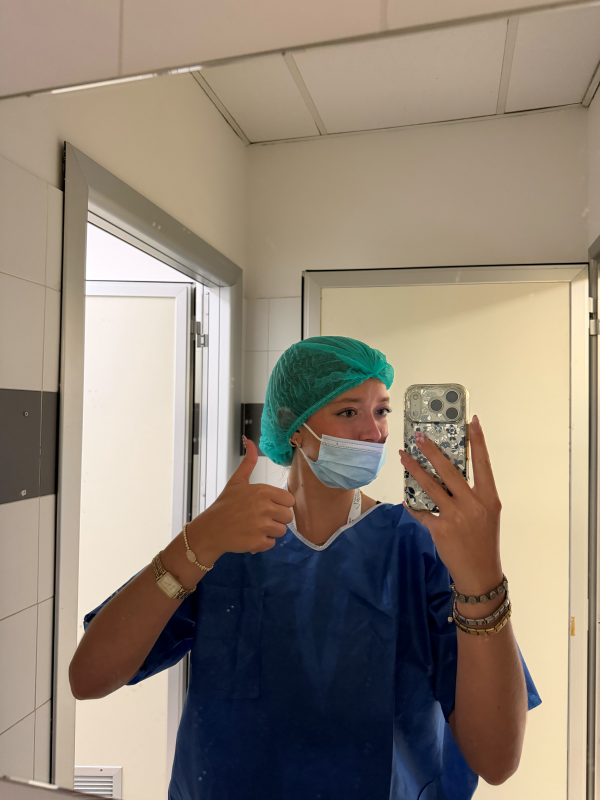 A study abroad student taking a selfie while wearing blue scrubs and giving a thumbs up to the camera