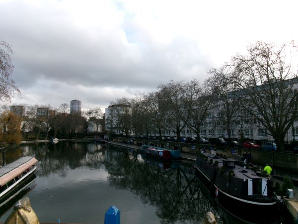 A small canal featuring houseboats and a row of orderly white houses to the righthand side