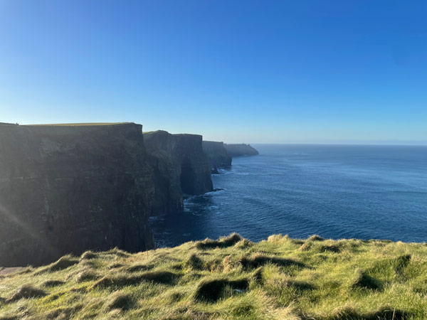 A cliff edge with a body of water and grass with Cliffs of Moher in the background
