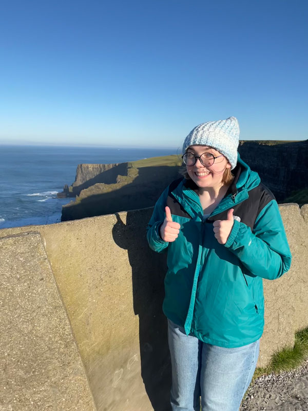 A study abroad student standing on a ledge with a thumbs up