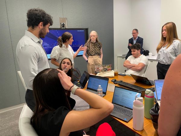 A group of pre-law students sitting and standing indoors, talking with each other and working on laptops