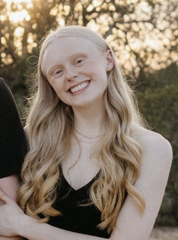 A study abroad student with long wavy blonde hair holding the arm of someone out of the shot and smiling at the camera
