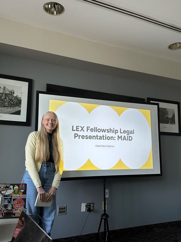 A pre-law student standing indoors in front of a large screen and smiling at the camera