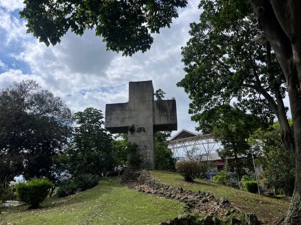 A large cross structure standing at the top of a small hill outdoors