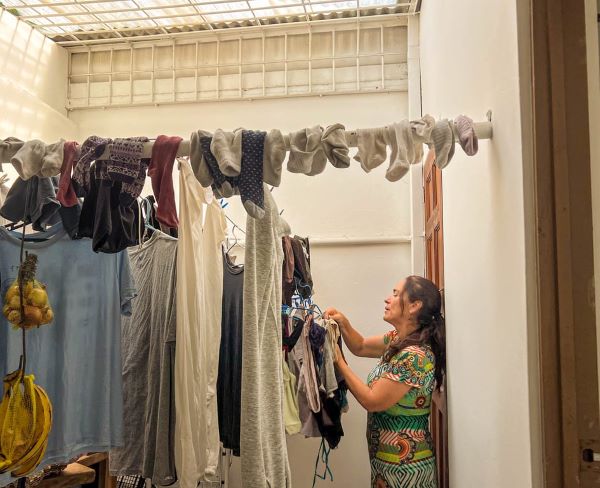 A person standing sideways to the camera and hanging up clothes on an indoor clothes line