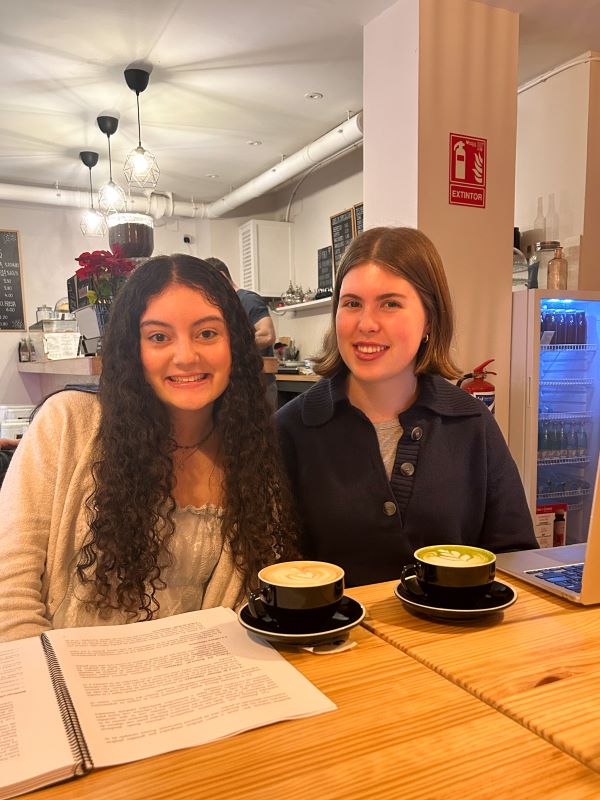 Two study abroad students sitting down behind two large cups of coffee and smiling at the camera