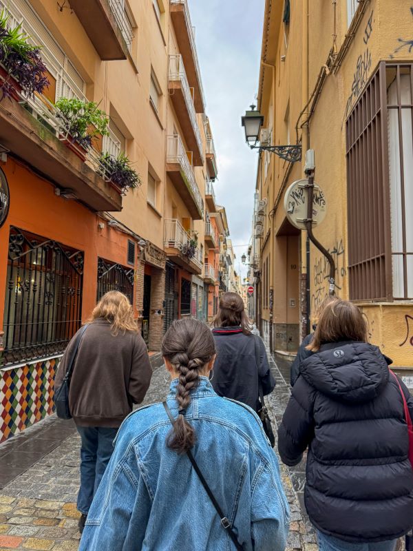 Four study abroad students seen from behind walking down a narrow city street