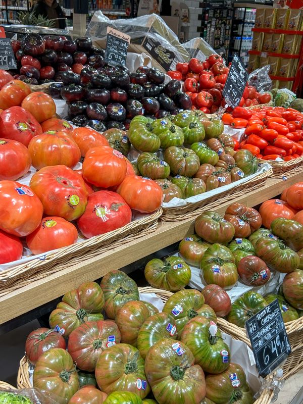 Multiple shelves featuring containers of fresh tomatoes in various shades of red, orange, and green