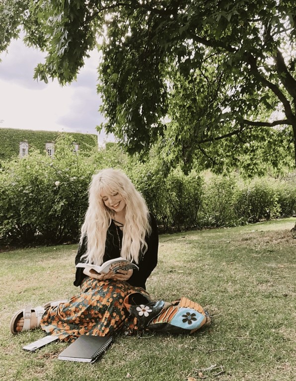A person reading a book smiling sitting on grass under a tree