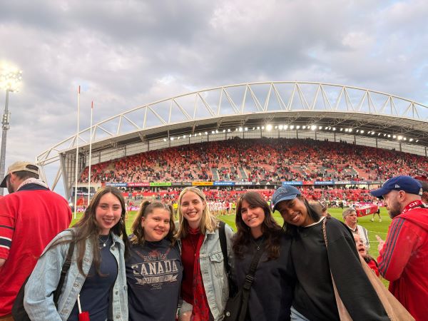 Five study abroad students standing in front of a large sports pitch with tall stands in the background