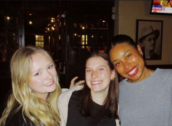 Three study abroad students in an indoor space, smiling at the camera with a photo of James Joyce on the wall in the background