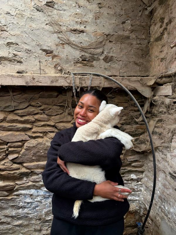 A study abroad student smiling at the camera and holding a small white lamb