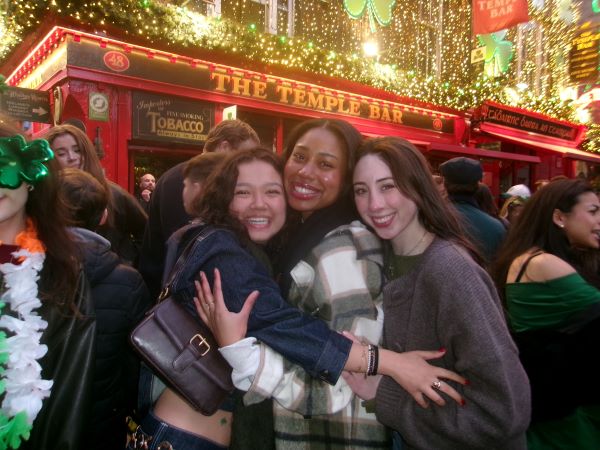 Three study abroad students standing in front of a building with the words