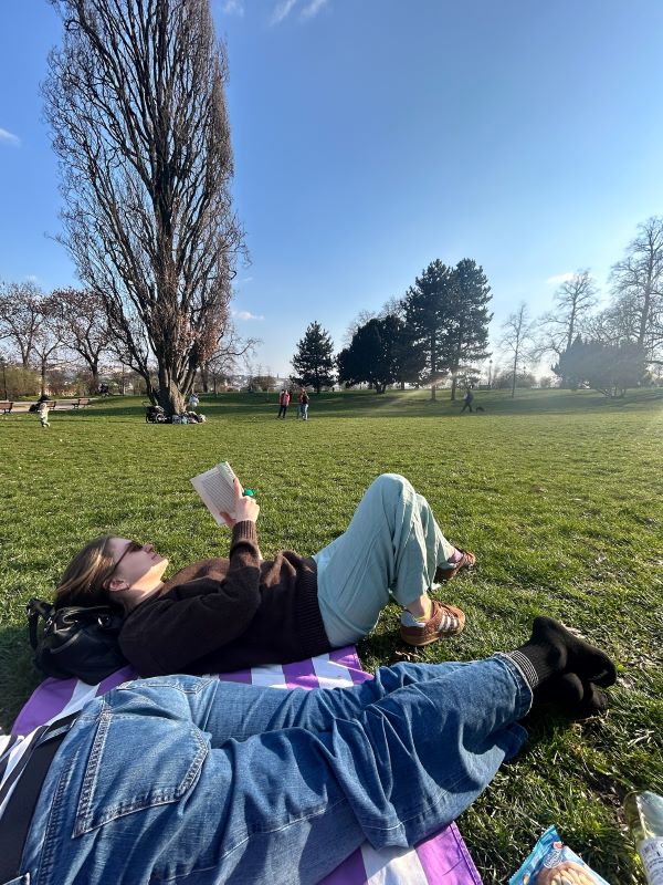 Two study abroad students lying on a blanket outdoors in a park with a large expanse of green grass