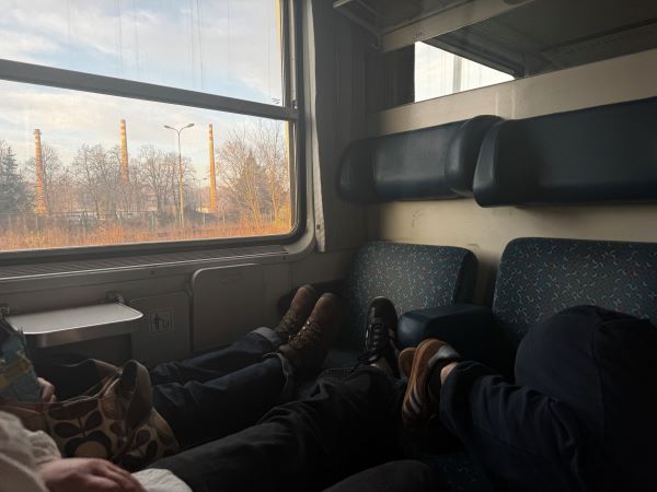 Several pairs of legs seen stretched out onto seats in an train carriage with views of the outdoors through a window to the left