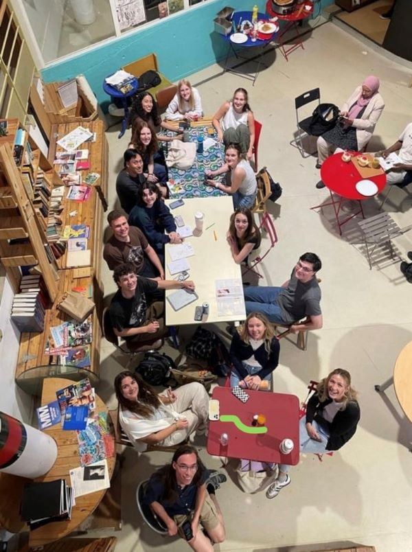 A group of study abroad students sitting around a table and smiling at the camera, as seen from a level above