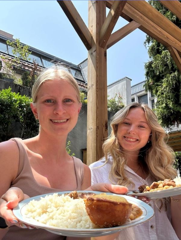 Two study abroad students holding plates of food and smiling at the camera