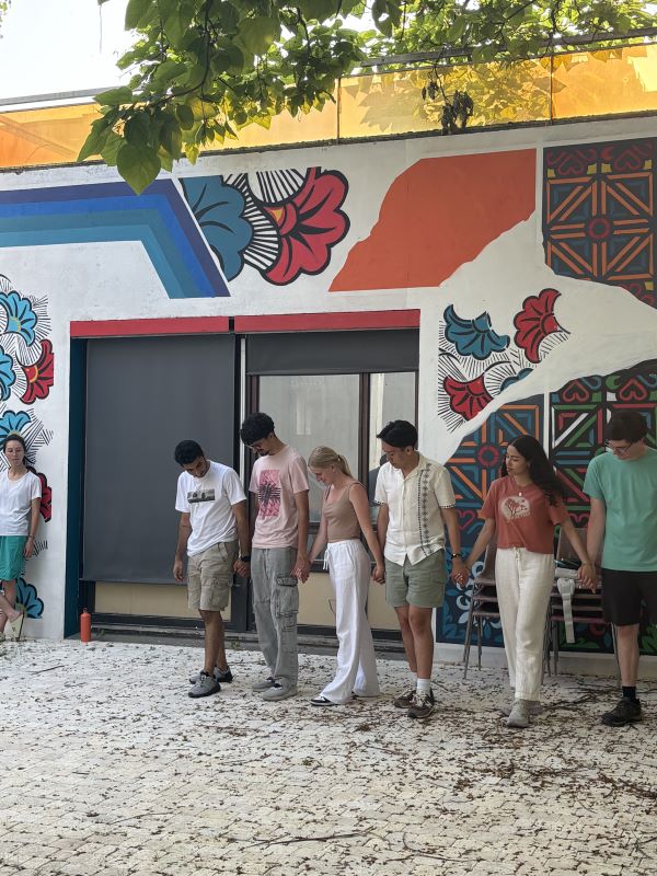 A group of study abroad students standing outside and holding hands while learning a dance