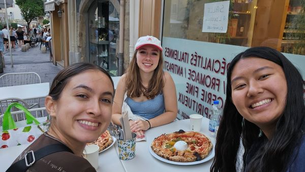 Three study abroad students taking a selfie sitting outdoors at a table with pizzas on it