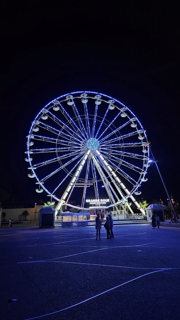 A large Ferris wheel seen at nighttime and lit up bright white against a black background sky