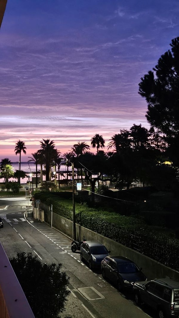 A street leading to a body of water seen in early morning under a pink and purple sunrise