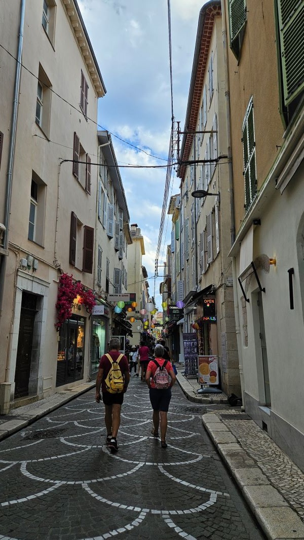 A narrow stone city street hemmed in by stone buildings and with people walking on it in both directions