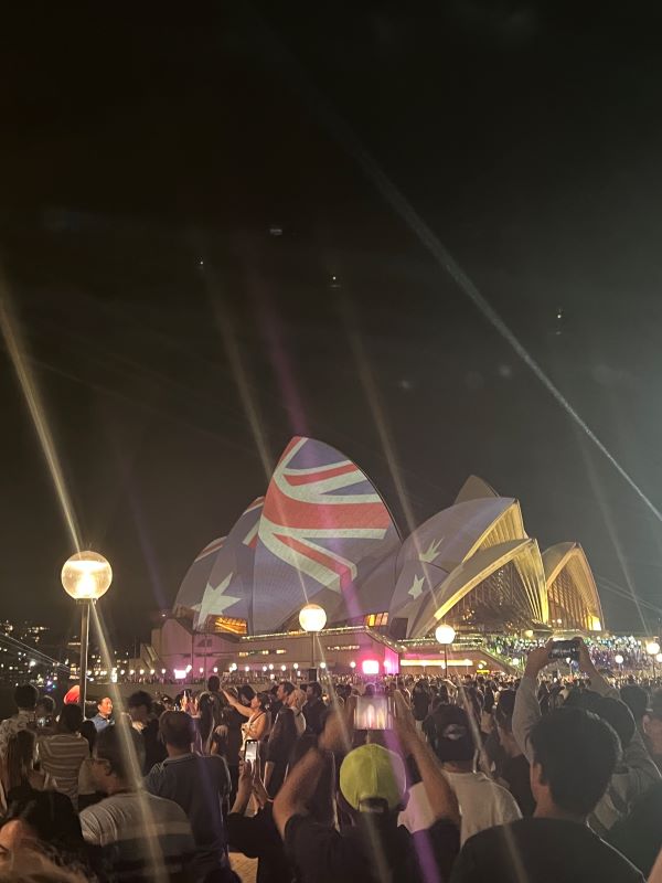 Crowd of civilians outside the Sydney Opera House with the Australian flag over roof