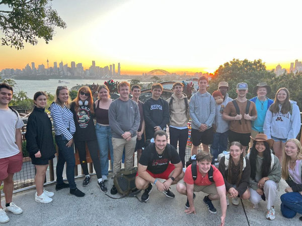 A group of study abroad students posing for a photo with city and water in background
