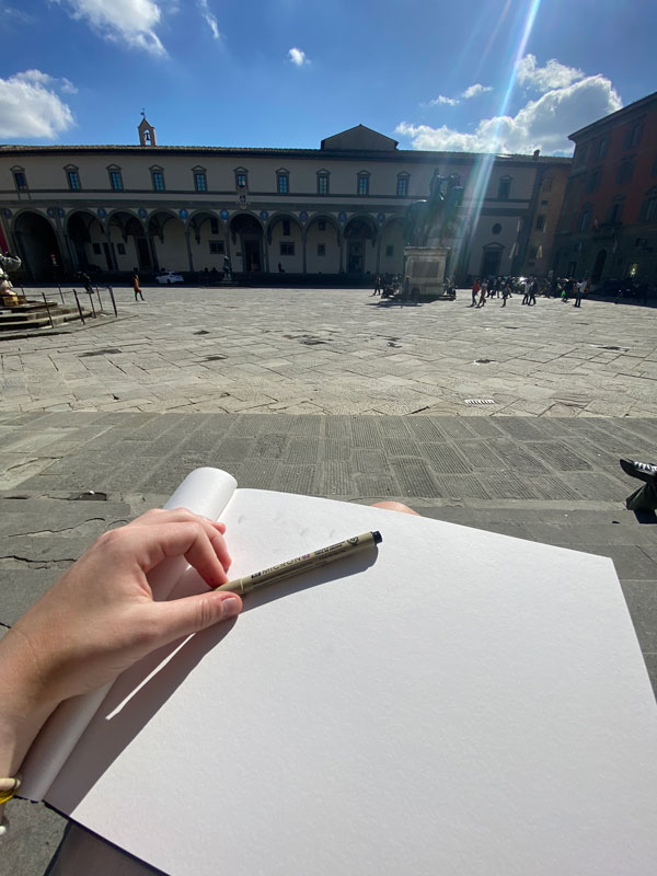 A study abroad student's hand resting on top of a blank white notebook page holding a pencil
