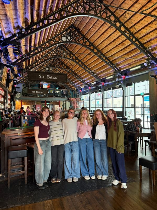 Six study abroad students standing together in an indoor space with a high ceiling and smiling at the camera