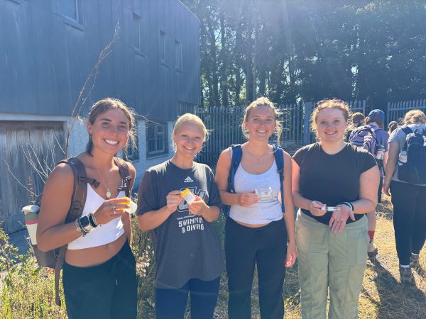 Four study abroad students standing outdoors and holding small plastic containers while smiling at the camera