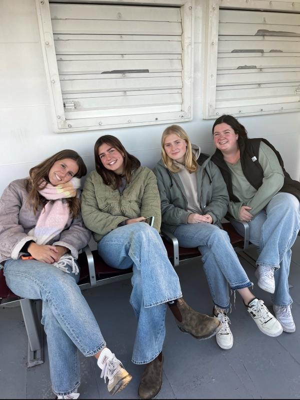 Four study abroad students sitting on ferry bench bundled in warm clothes