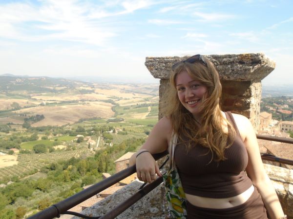A study abroad student leaning on a stone wall and smiling at the camera with a vast green landscape in the background