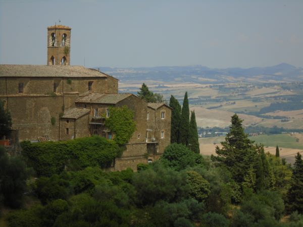 A brown stone building surrounded by trees in the foreground with a vast green landscape in the background