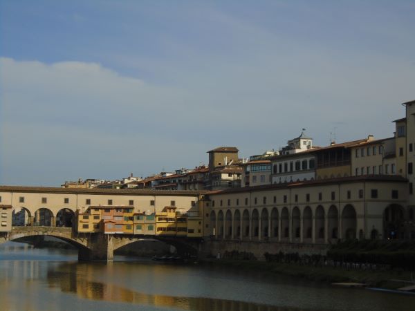 Sand-colored city buildings alongside a river, with some stretching out atop a bridge across the river