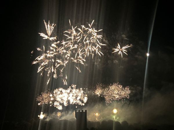 Bright white firework explosions seen against a dark night sky above a tower structure