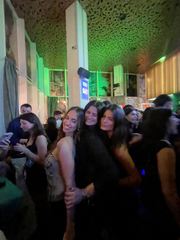 Three study abroad students standing close together in an indoor space, smiling with their eyes closed