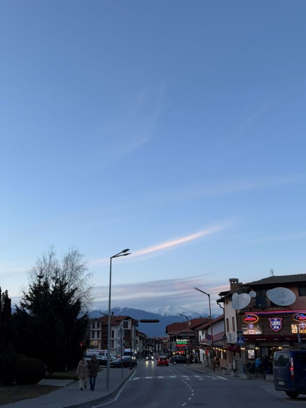 A street below a blue evening sky with buildings on either side of the road and mountains in the distance