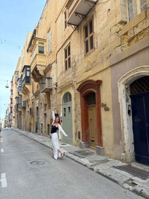A study abroad student standing alone on a city street, smiling at the camera with their hands raised in a joyful way