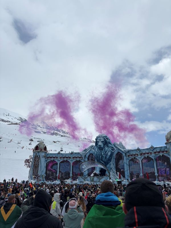 A large group of people in front of a stage featuring a large fake lion statue with purple smoke and mountains behind it