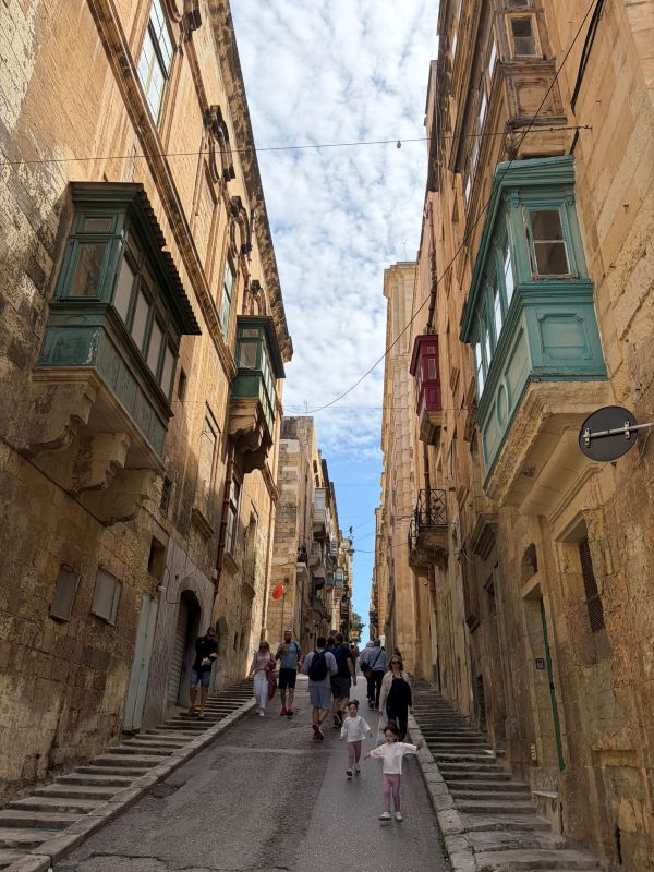 A steep city street with people walking either way on it, as seen from the bottom
