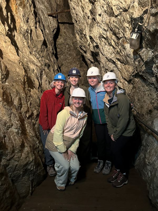 Five study abroad students wearing white hard hats and smiling at the camera in a rocky indoor setting