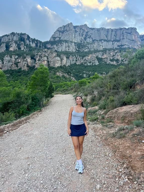 A study abroad student smiling at the camera and standing on a rocky path with a large mountainous structure in the background