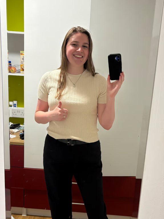 A study abroad student wearing a yellow shirt and black trousers and taking a selfie in a full-length mirror