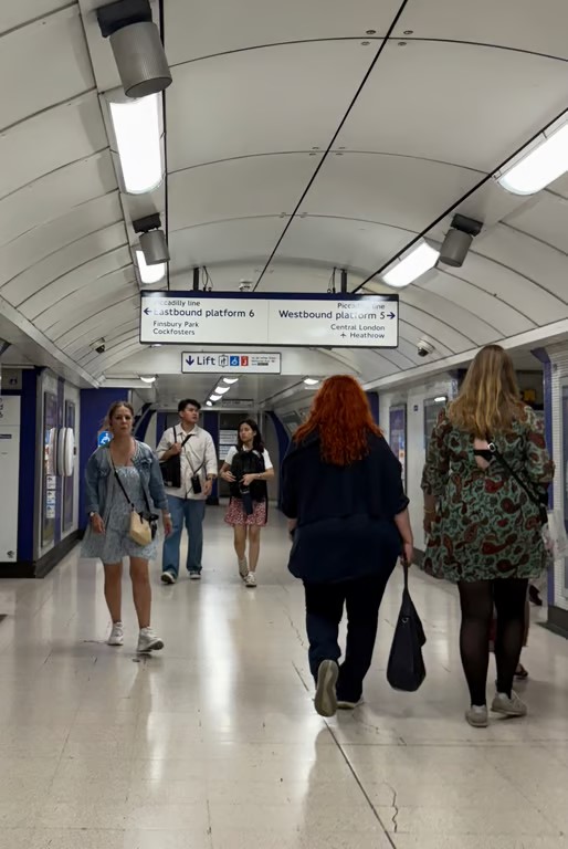 Several people walking away from and toward the camera in an indoor public transportation setting