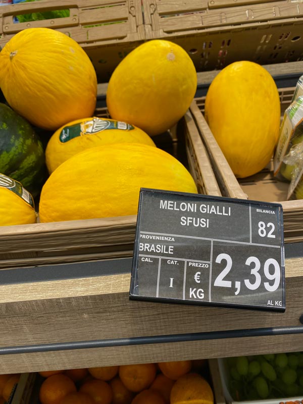 A sign on a shelf with melons