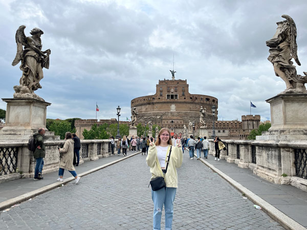 A study abroad student standing on Castel Sant'Angelo with a stone building in the background