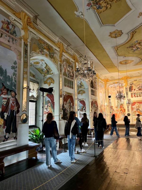A group of study abroad students seen from behind inside a large ornate room filled with paintings