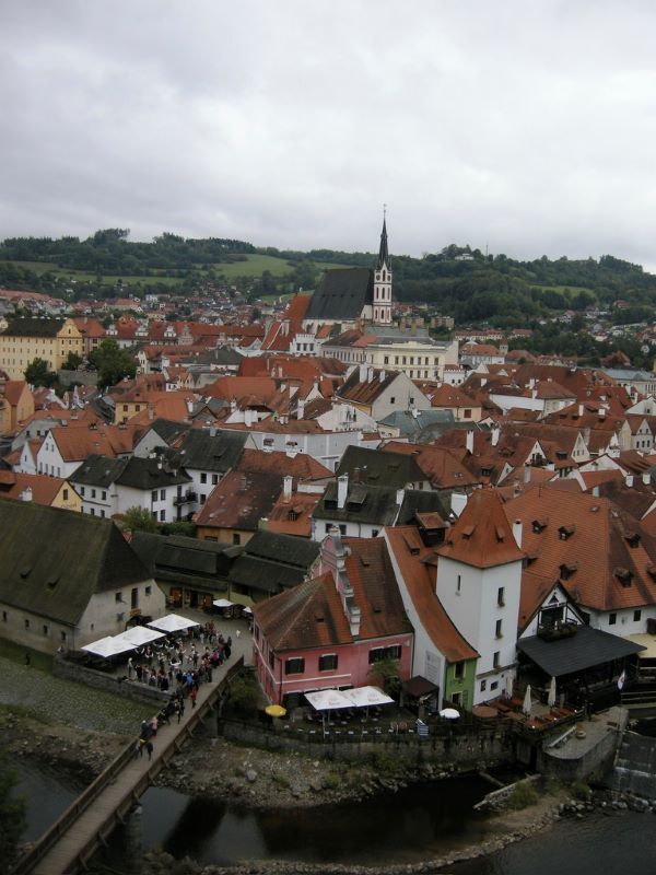 A view from above of a cluster of buildings, many with rusty red roofs, and a large church steeple in the past
