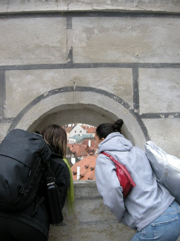 Two study abroad students seen from behind looking through a small curved window at town buildings